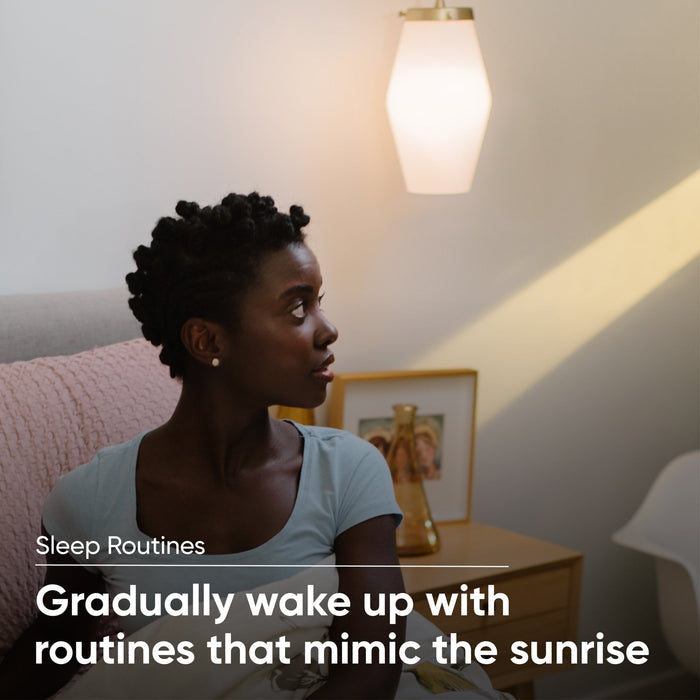 A woman sitting on a bed with a Wyze Bulb White on the nightstand.
